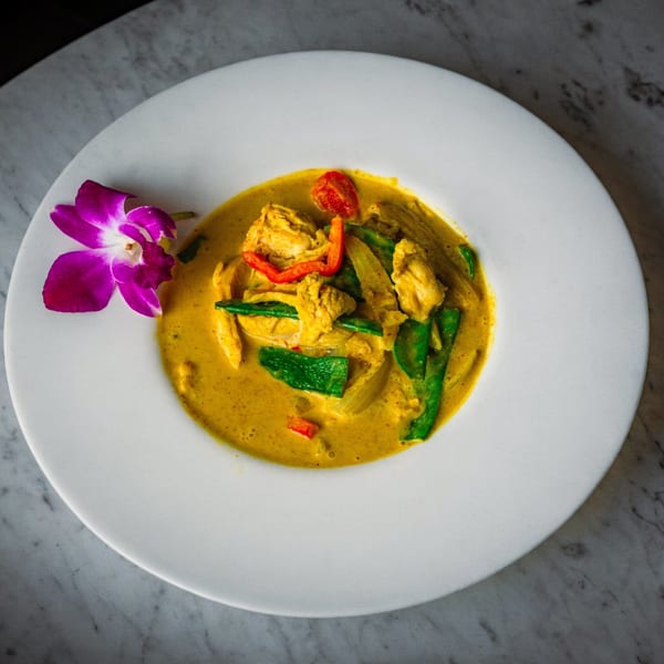 A vibrant yellow curry with chicken, green beans, and red peppers, garnished with a purple orchid.